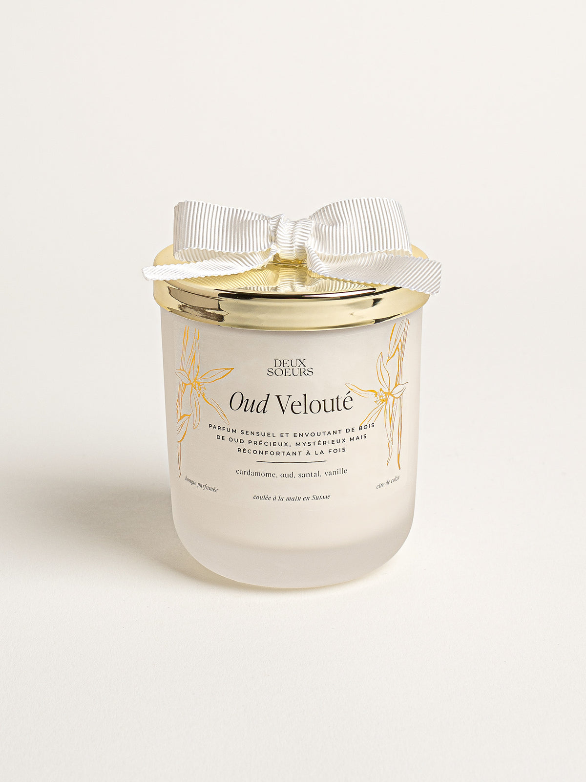 A frosted glass jar candle with a gold lid and a white satin bow, labeled 'Oud Velouté' by Deux Soeurs, on a clean off-white background. 