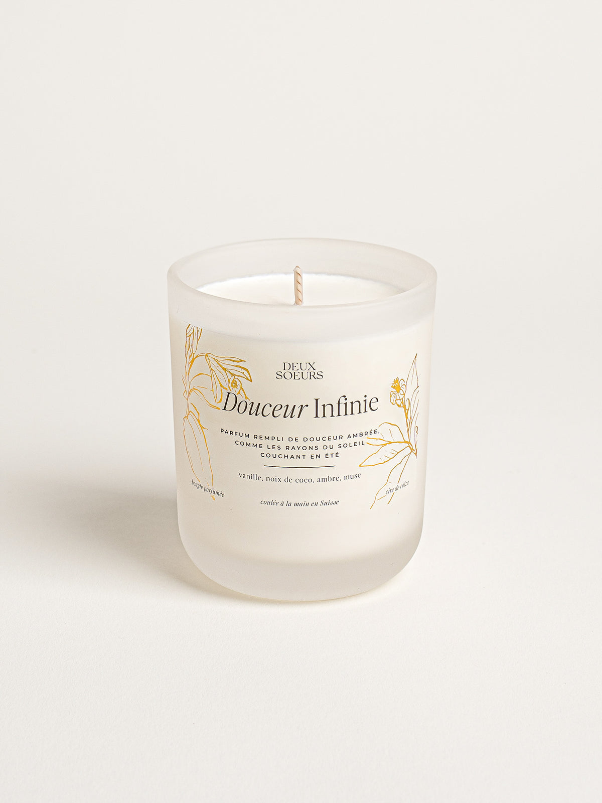 A frosted glass jar candle with a single wick, featuring a white label with gold botanical illustrations and the brand name 'Deux Soeurs' and scent name 'Douceur Infinie'.